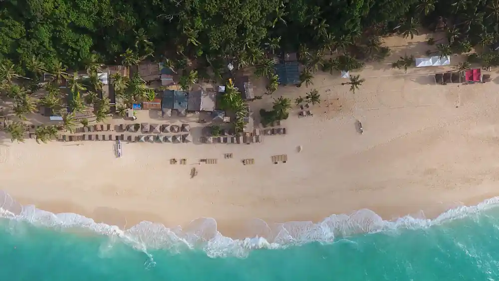 an aerial view down onto a beach lined with thatched huts