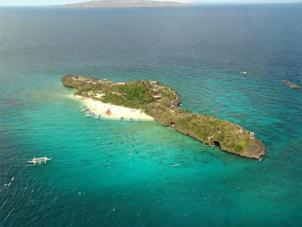 an aerial view of a small green island ringed by pale shallows