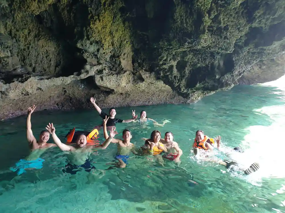 a dozen guests in life vests swimming together at the mouth of a sea cave