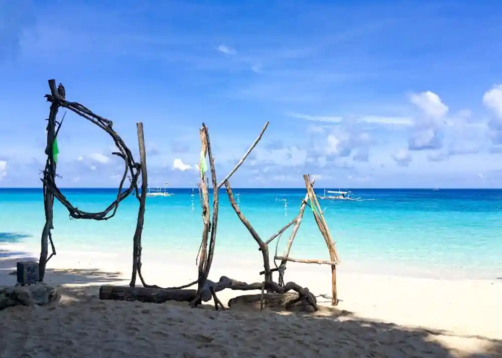 a driftwood frame standing on white sand against turquoise water and moored boats