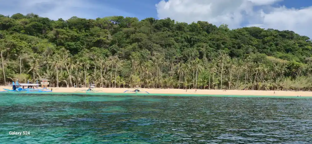 a green island with a pale beach and a boat drawn up on the sand