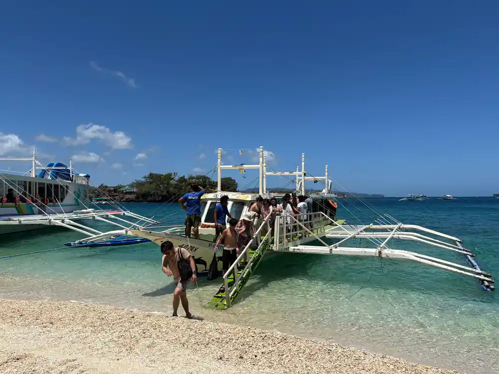 guests walking down the gangplank from the outrigger onto the beach