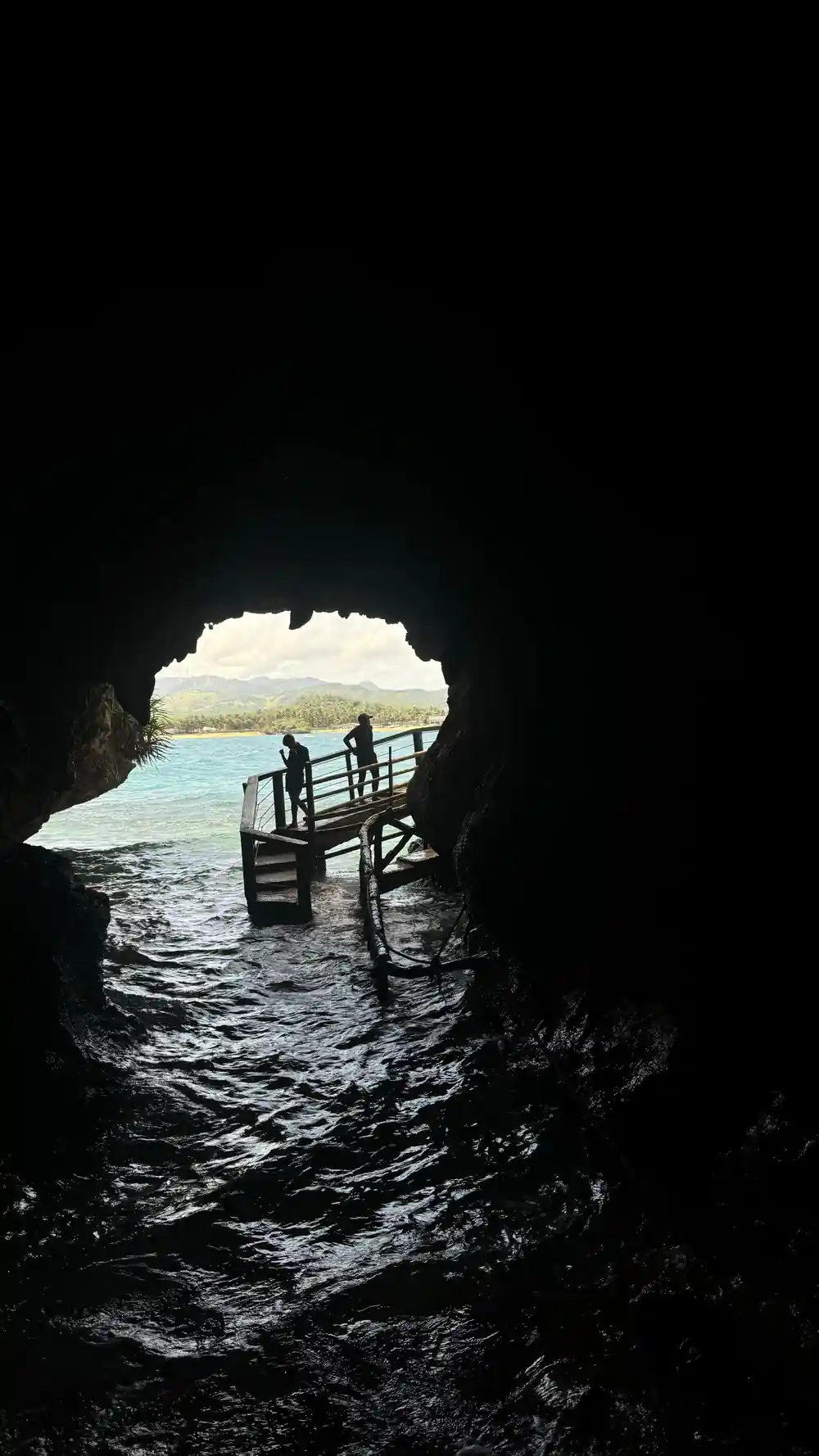 the mouth of a sea cave with a wooden walkway and two figures silhouetted