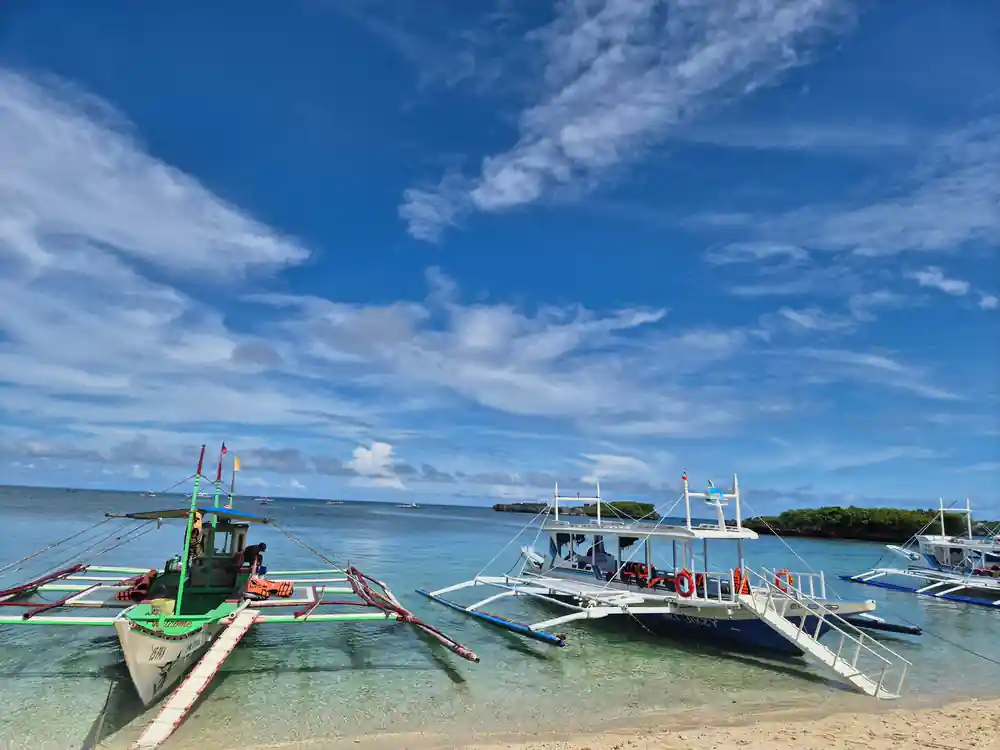 outrigger boats moored off a beach under a wide blue sky
