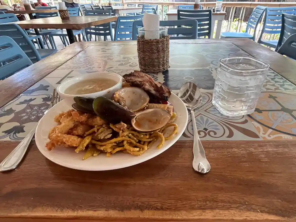a plate of clams, fish and chips on a restaurant table by the water