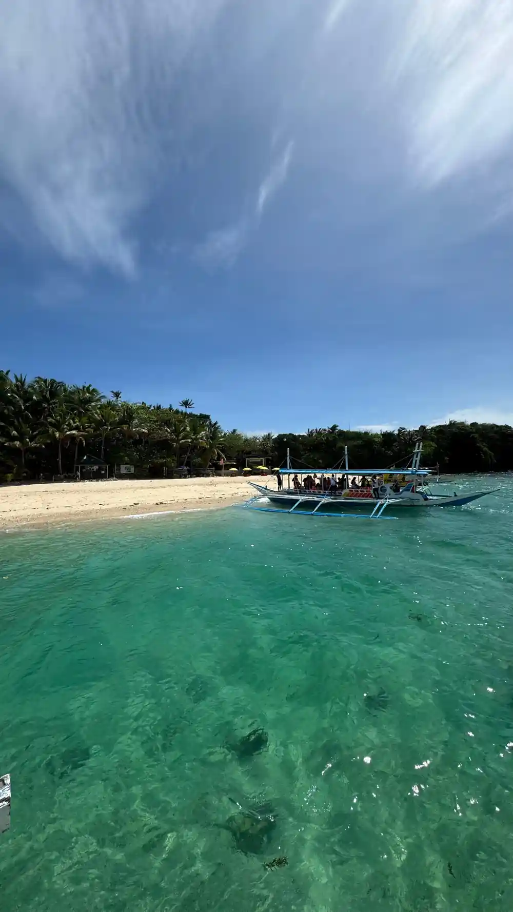 a sandbar with an outrigger boat drawn up and green water either side