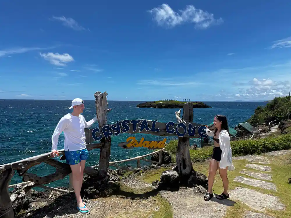 two guests posing at the driftwood Crystal Cove Island sign
