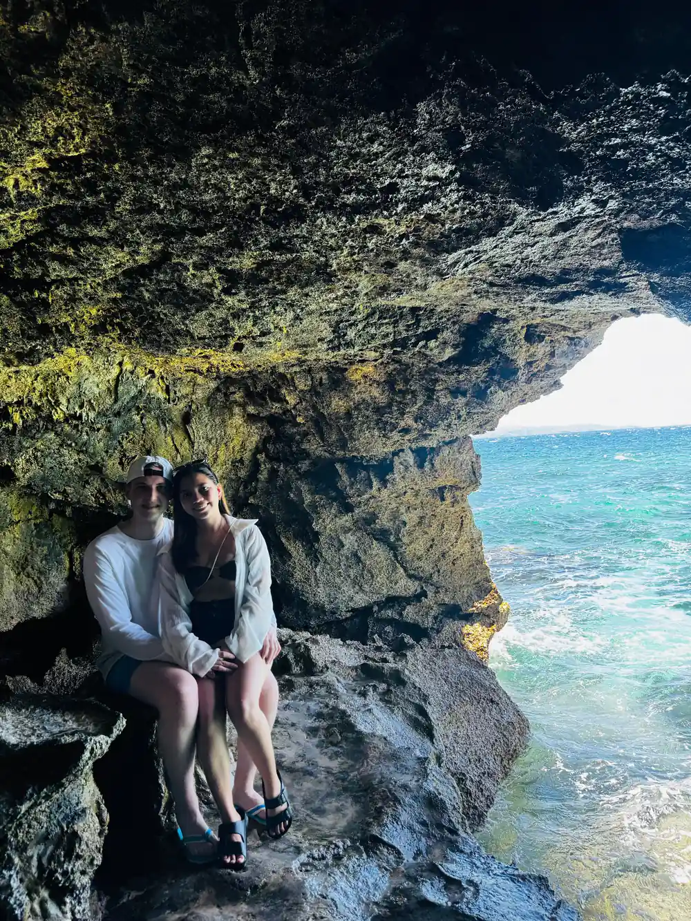 two guests sitting inside a rock arch above turquoise water