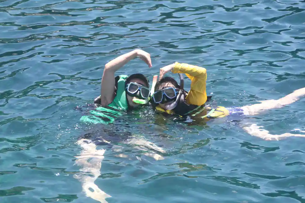 two snorkellers making a heart shape with their arms at the surface