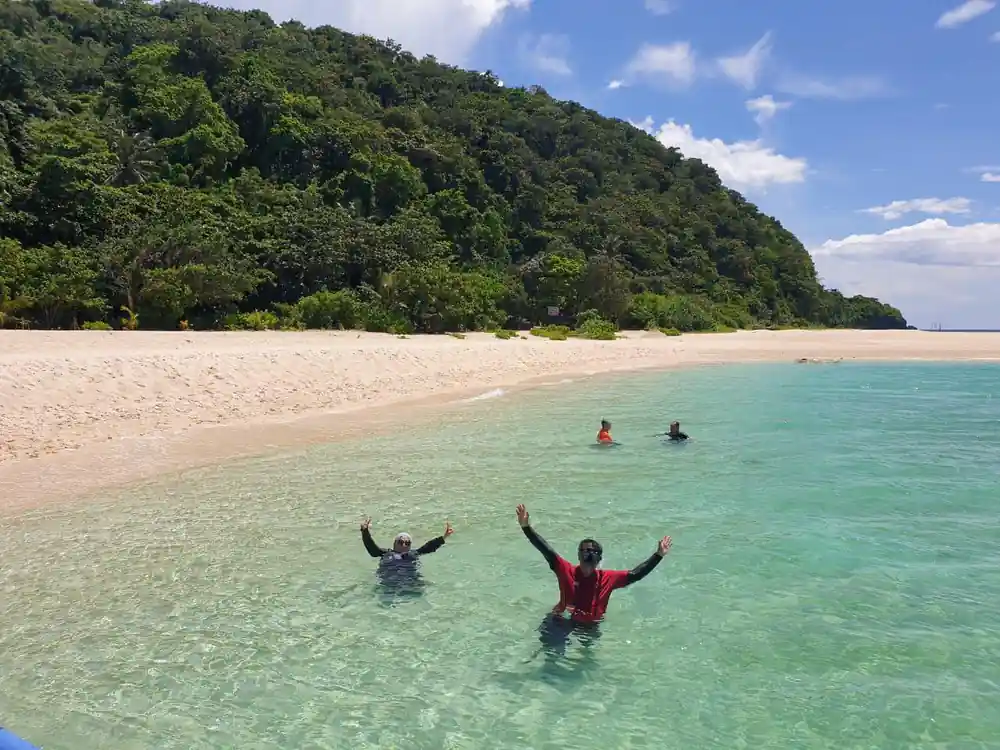 two swimmers waving from the shallows off a wooded island beach