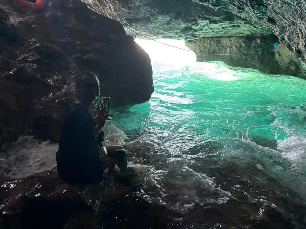a visitor photographing bright green water surging into a rocky inlet
