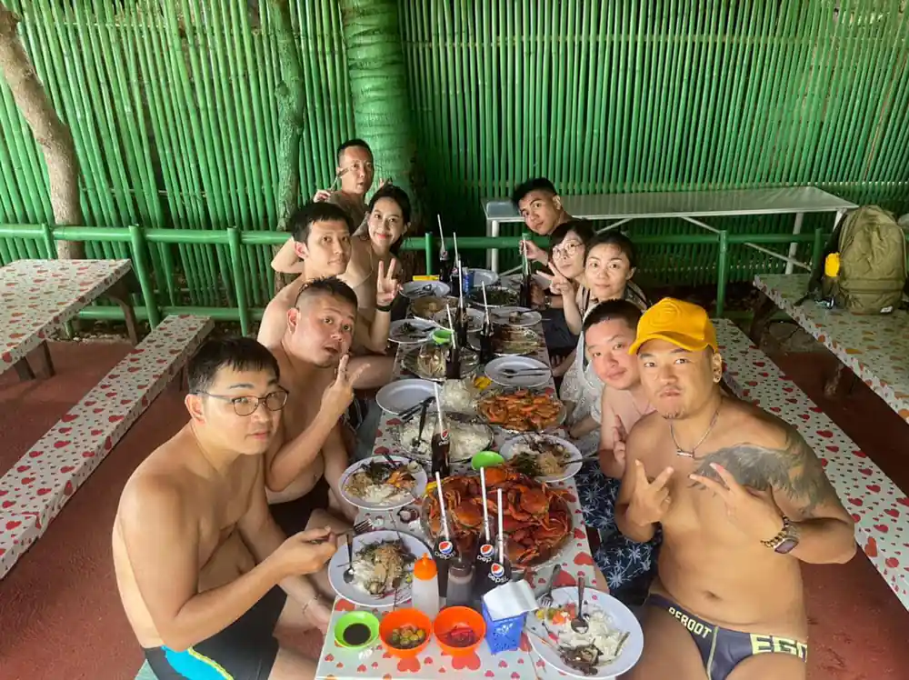 the whole group gathered around a long table of food under a bamboo roof
